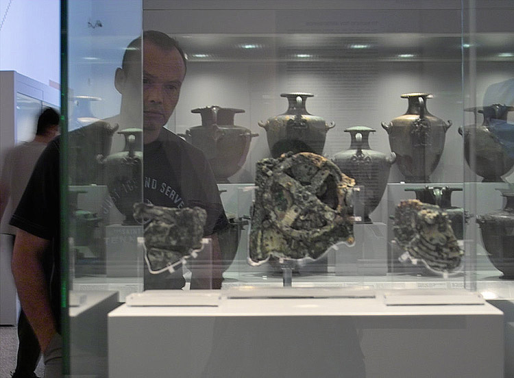 The Antikythera Mechanism on display at the National Archaeological Museum, with conservator Gerassimos Makris. (Photo by Yanis Bitsakis)